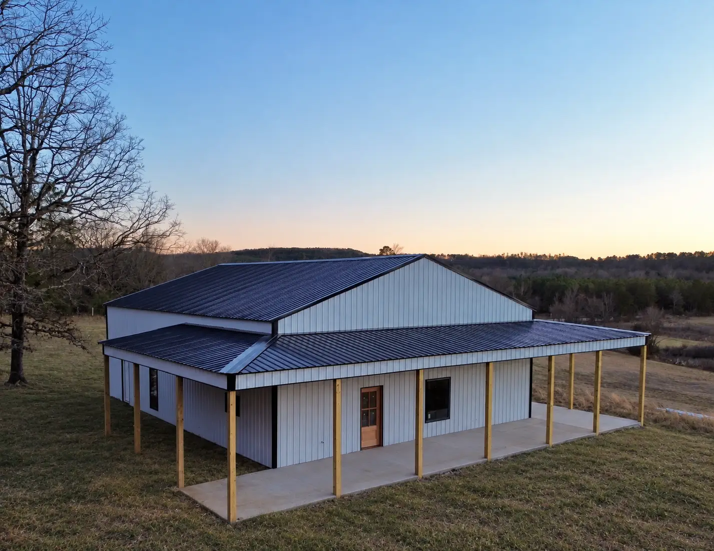 Metal-roof barndominium with a wraparound porch at dusk, built by C&M Innovations in the Arkansas River Valley
