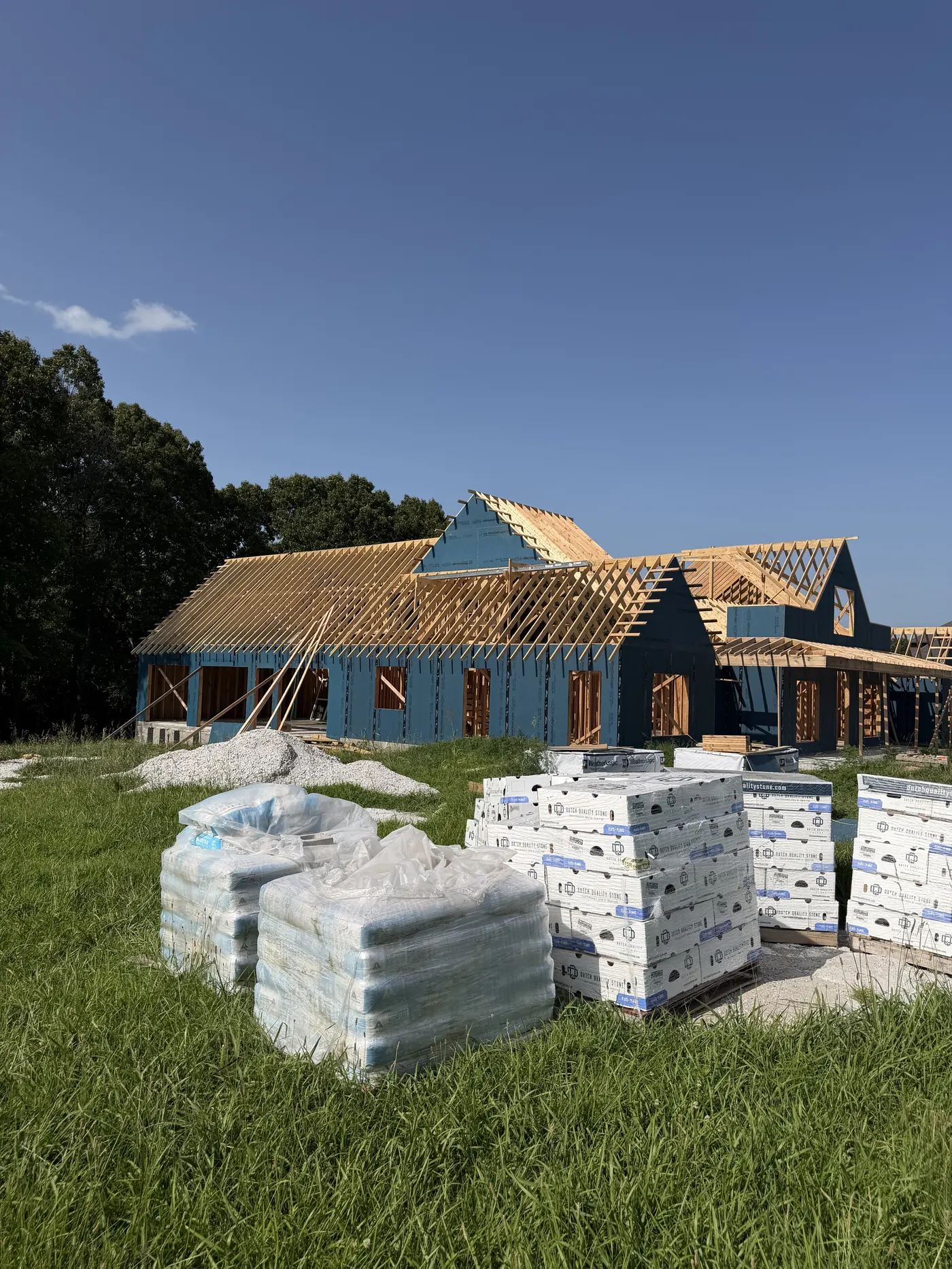 Large custom home under construction with steep gables and roof trusses being set