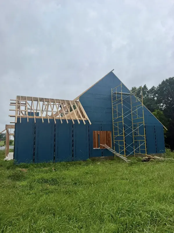 Roof framing going up on a blue-wrapped gable home