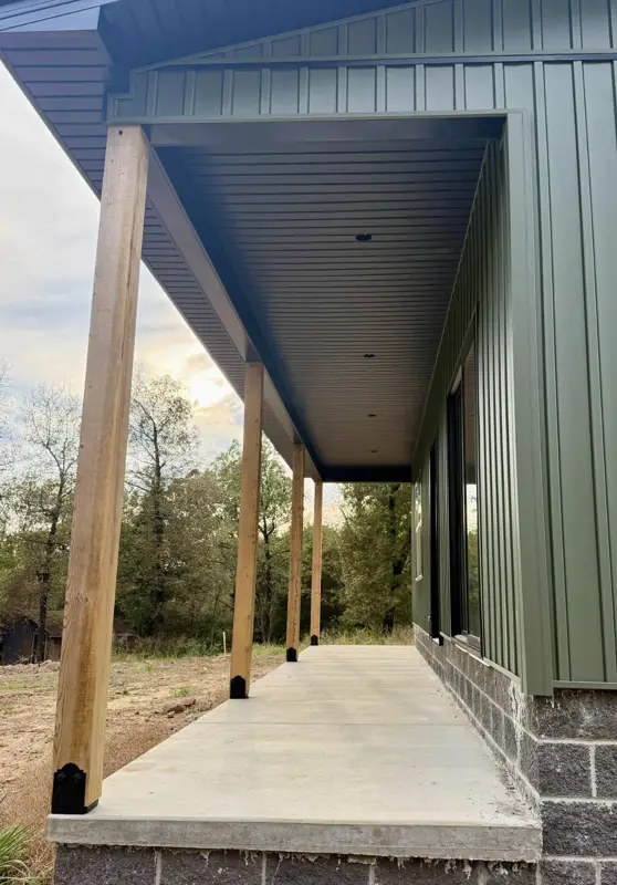 Corner of a green metal-siding porch with timber posts