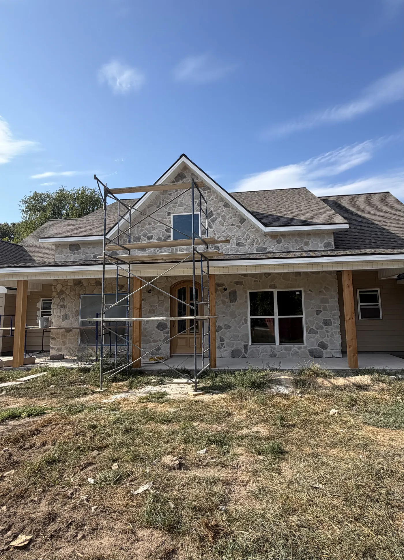 Stone and tan-siding custom ranch home with timber porch posts built by C&M Innovations